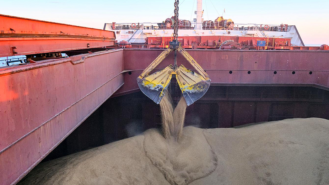 Der Laderaum eines großen Frachters wird von einer Kranschaufel mit Getreide befüllt