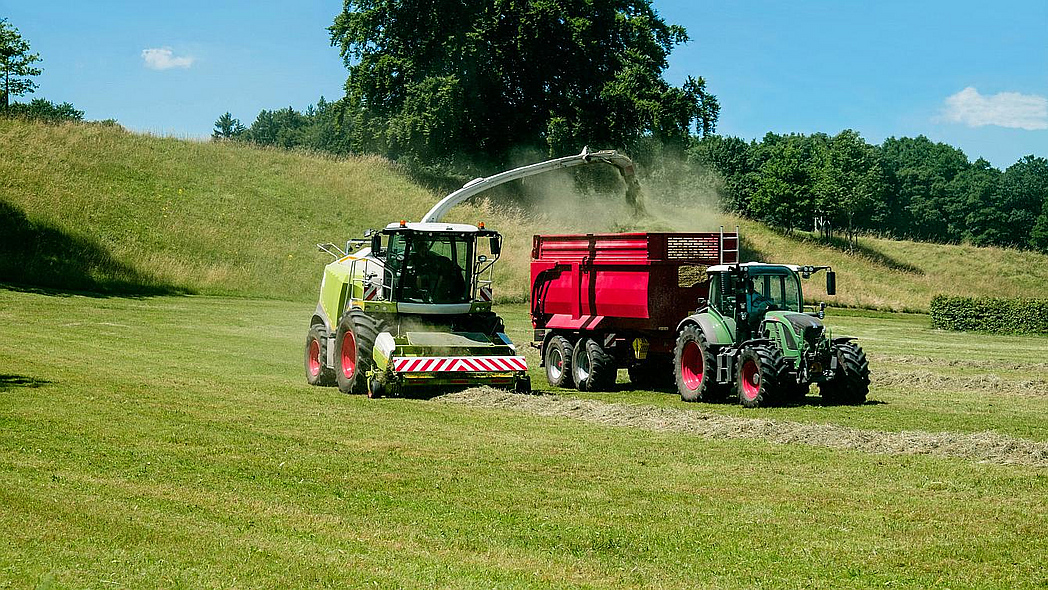 Ein Traktor mit Anhänger und ein Häcksler bei der Heuernte