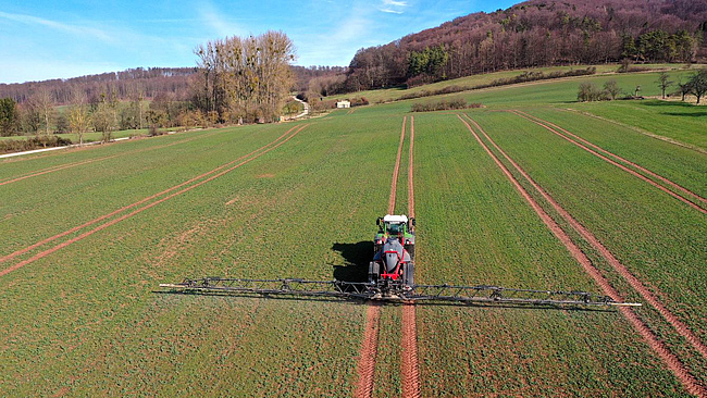 Luftbild eines Traktors mit Pflanzenschutzpritze auf einem Rapsfeld
