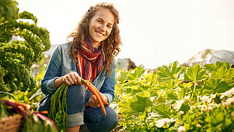 Lachende junge Frau bei der Ernte von frischem Gemüse mit Möhren in der Hand.