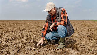Ein Landwirt kniet auf dem Acker und prüft den Boden
